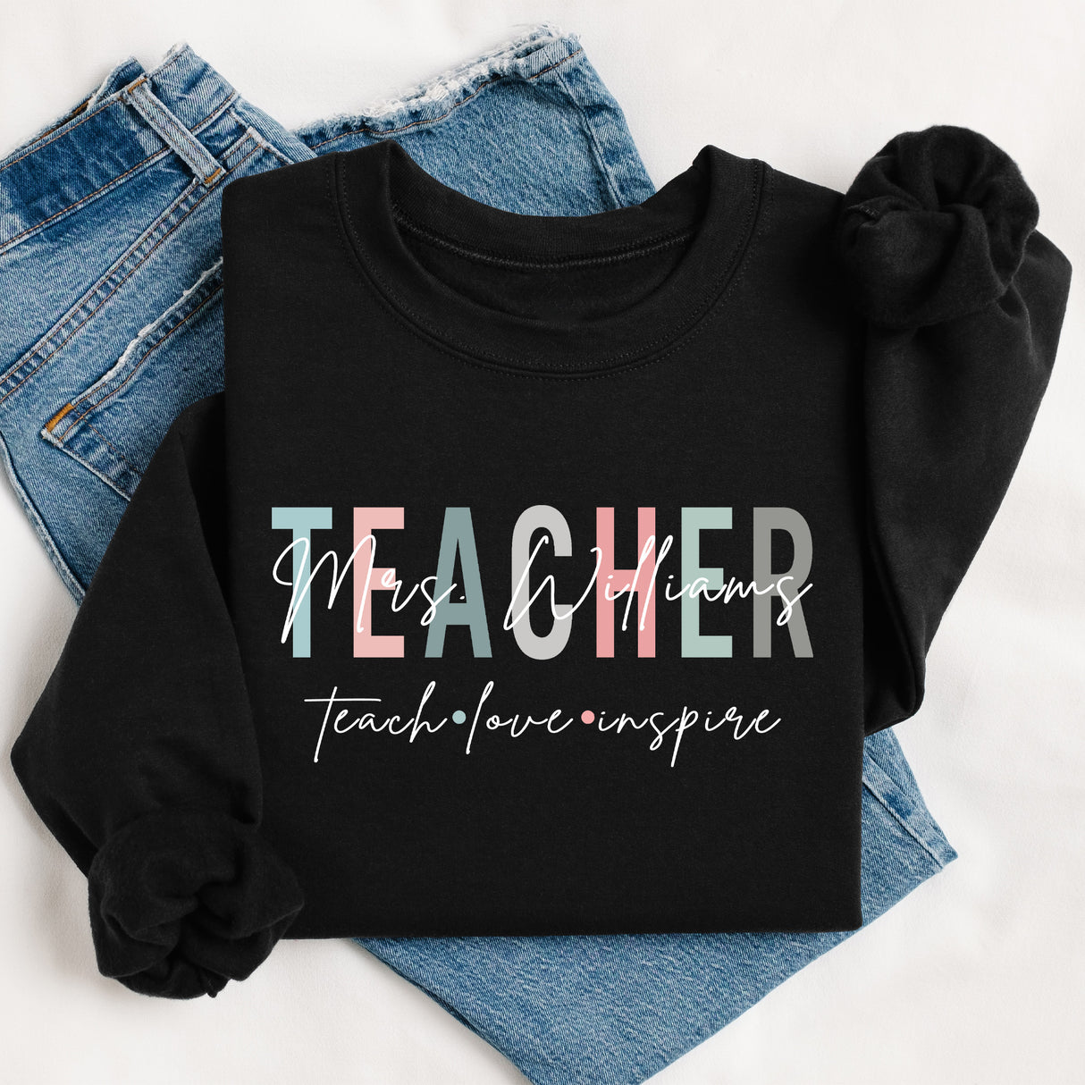 Flat lay of personalized Teach Love Inspire teacher sweatshirt with last name, custom crewneck teacher appreciation gift.