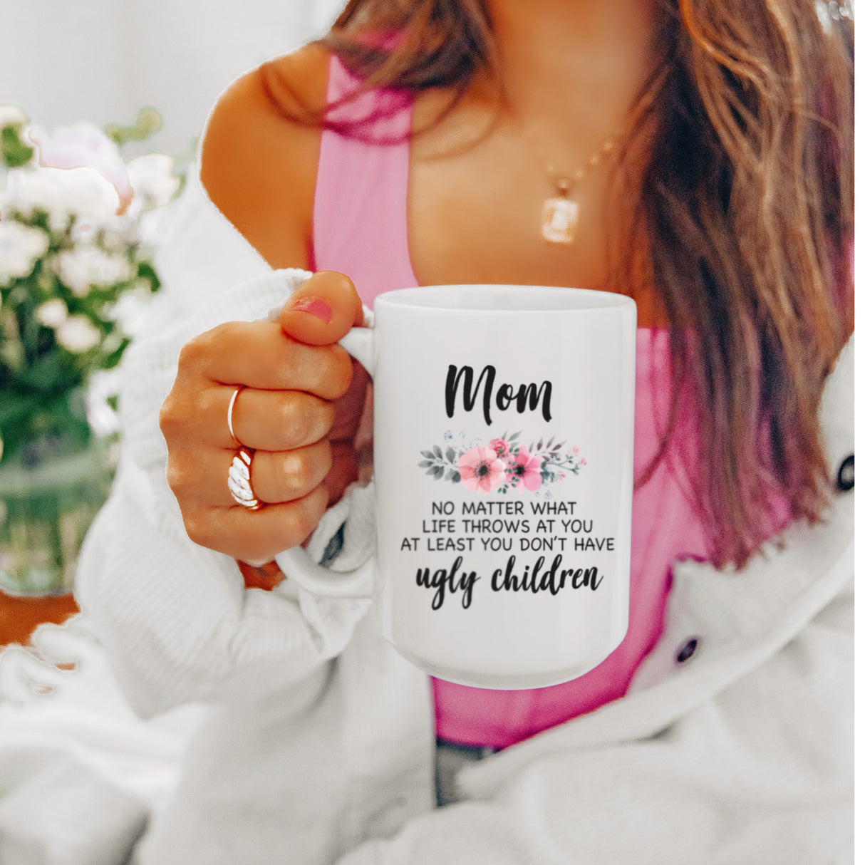 Smiling woman holding a humorous white coffee mug for mom with floral design which is an ideal birthday or Christmas gift for mom.