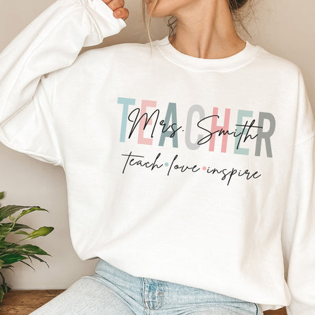 Women wearing personalized teacher sweatshirt with Teach Love Inspire text and custom last name, the perfect teacher gift for women.