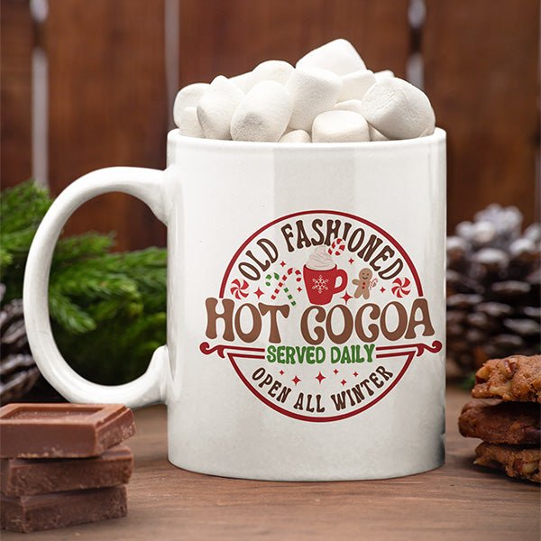 Old fashioned hot cocoa mug with Christmas graphic design that includes candy cane, gingerbread man and peppermint candy.
