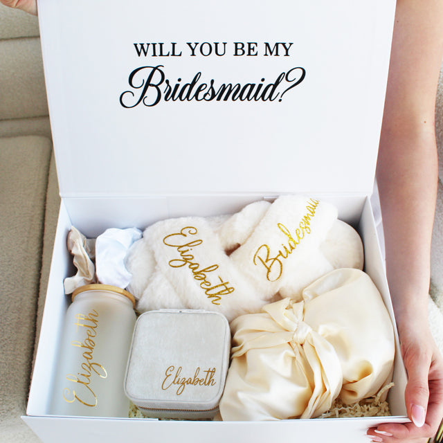 Bridal party gift box with personalized items including a jewelry box, robe, slippers, and drinkware for bridesmaids.