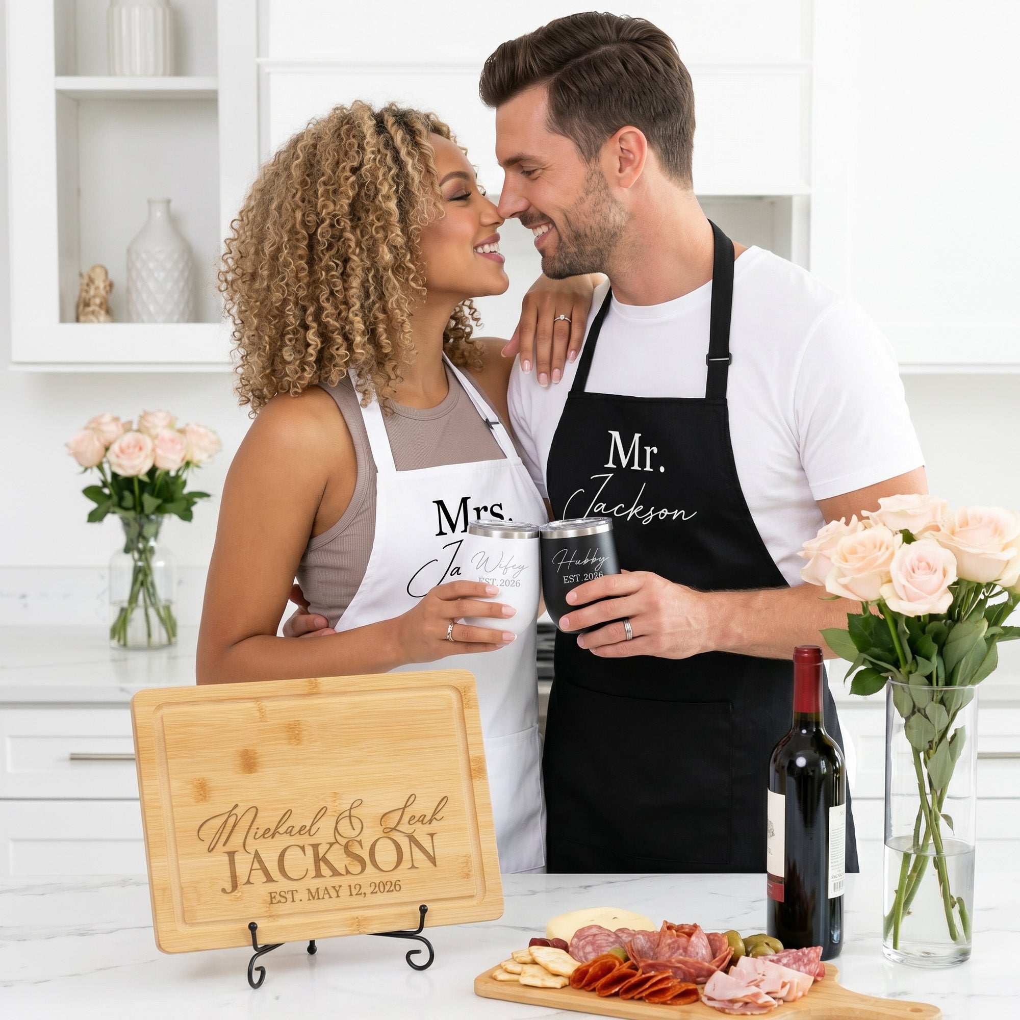 Couple in matching aprons with personalized cutting board and matching wifey and hubby wine tumblers. The gift set items can be customized with couples names and last name and their established date.