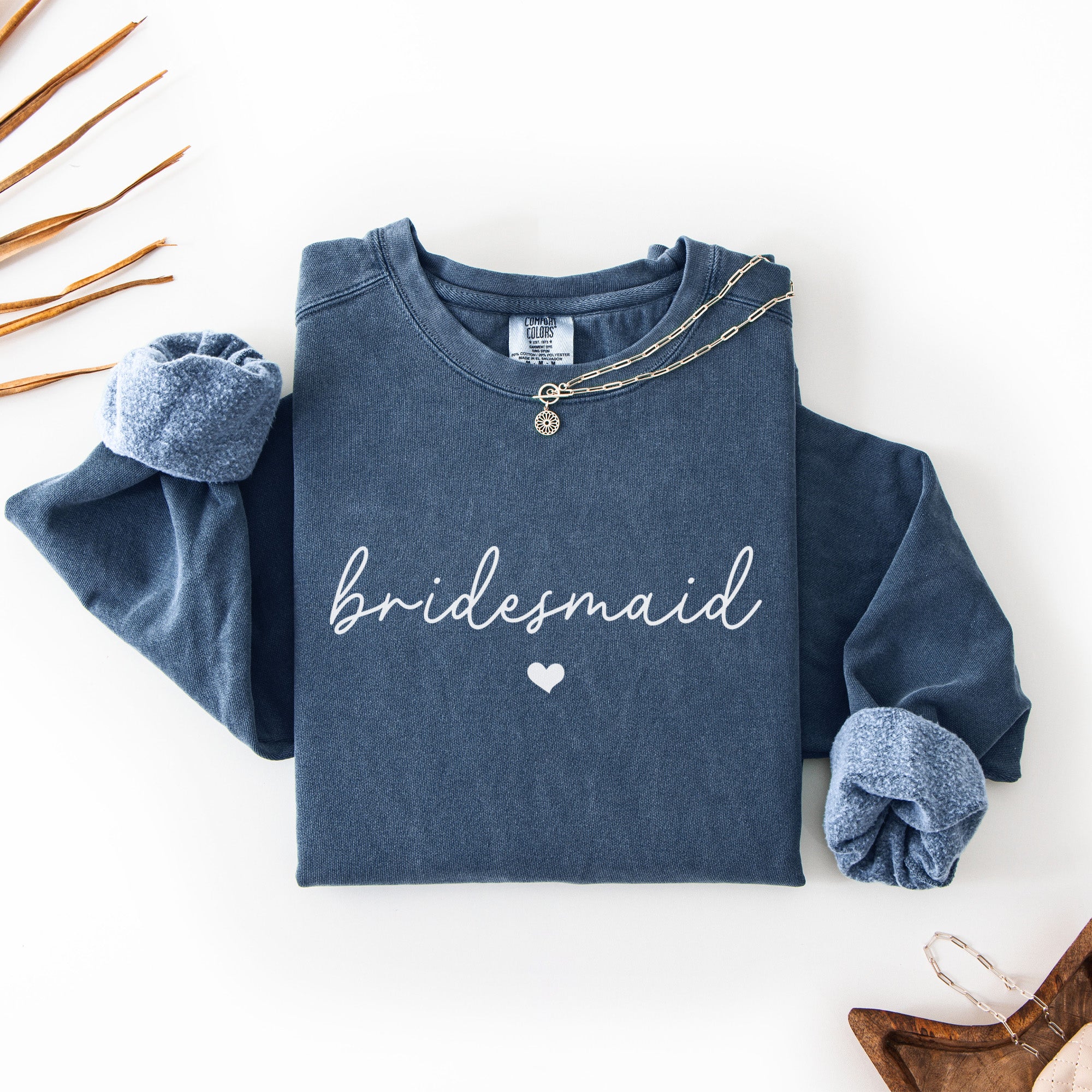 Flat lay of custom Comfort Colors bridal party sweatshirts customized with bride and bridesmaid names. Perfect for bachelorette party shirts and gift boxes.