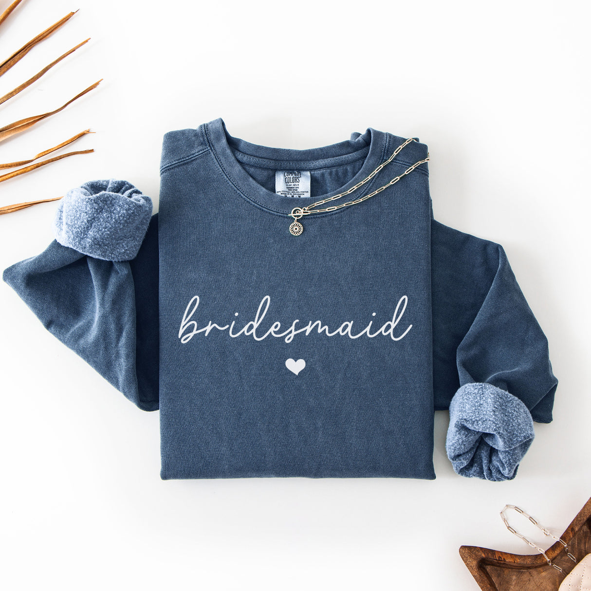 Flat lay of custom Comfort Colors bridal party sweatshirts customized with bride and bridesmaid names. Perfect for bachelorette party shirts and gift boxes.