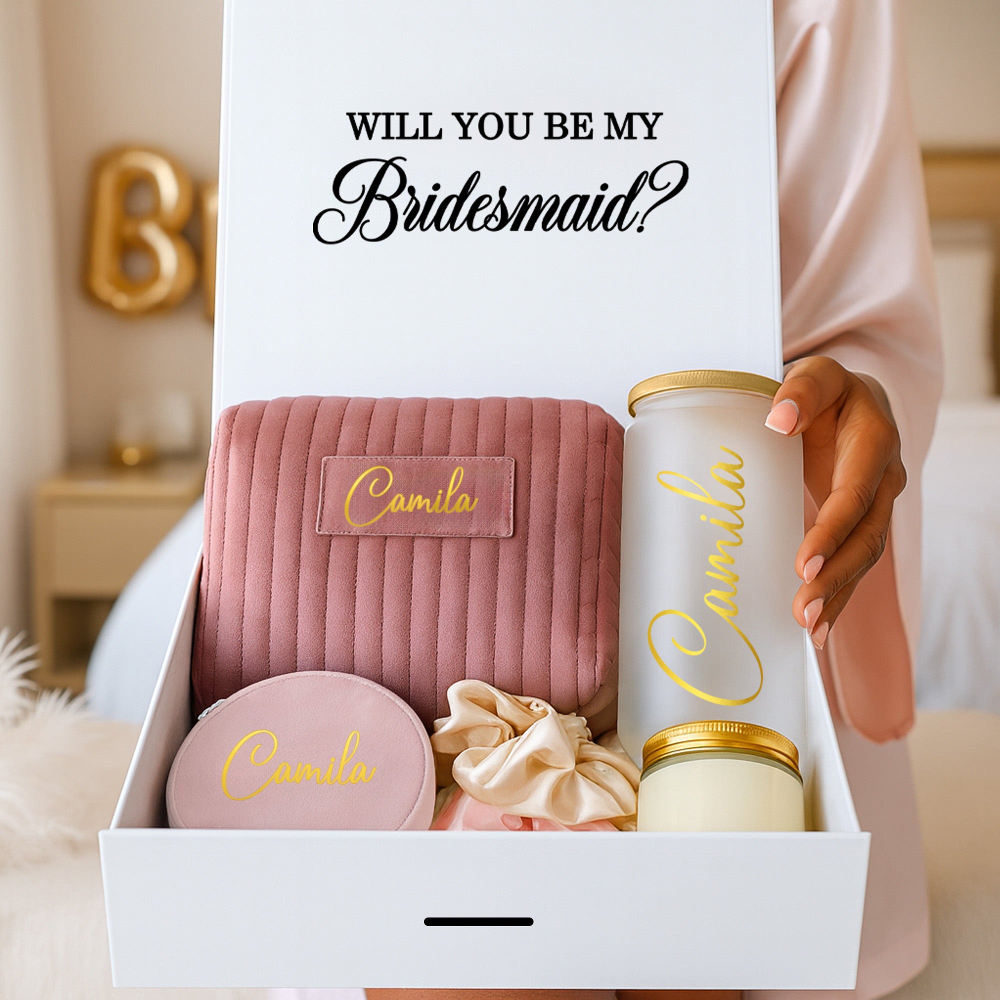 Young woman holding a cute, personalized bridesmaid proposal box with a custom frosted glass tumbler, a personalized bridesmaid makeup bag, a personalized jewelry box, 2 scrunchies and a gold lid candle. Perfect gifts for your bridal party.