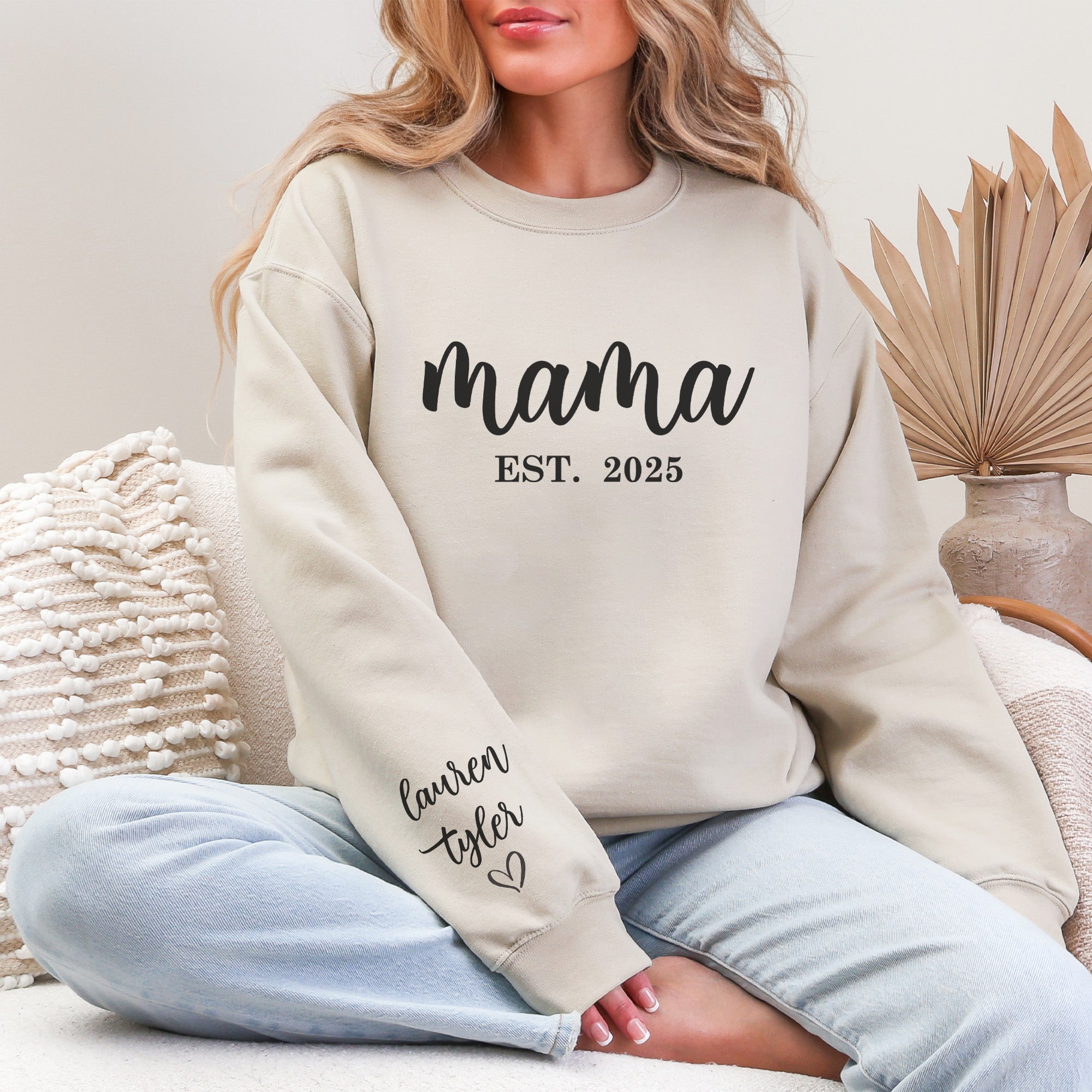 Woman wearing a cozy personalized Mama sweatshirt, featuring Mama on the chest and children’s names written along the sleeve. Personalized sweatshirt with kids’ names on the sleeve, worn by a smiling mom. 