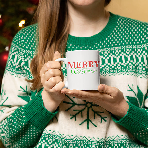 Woman holding Merry Christmas mug while wearing a green Christmas sweater.